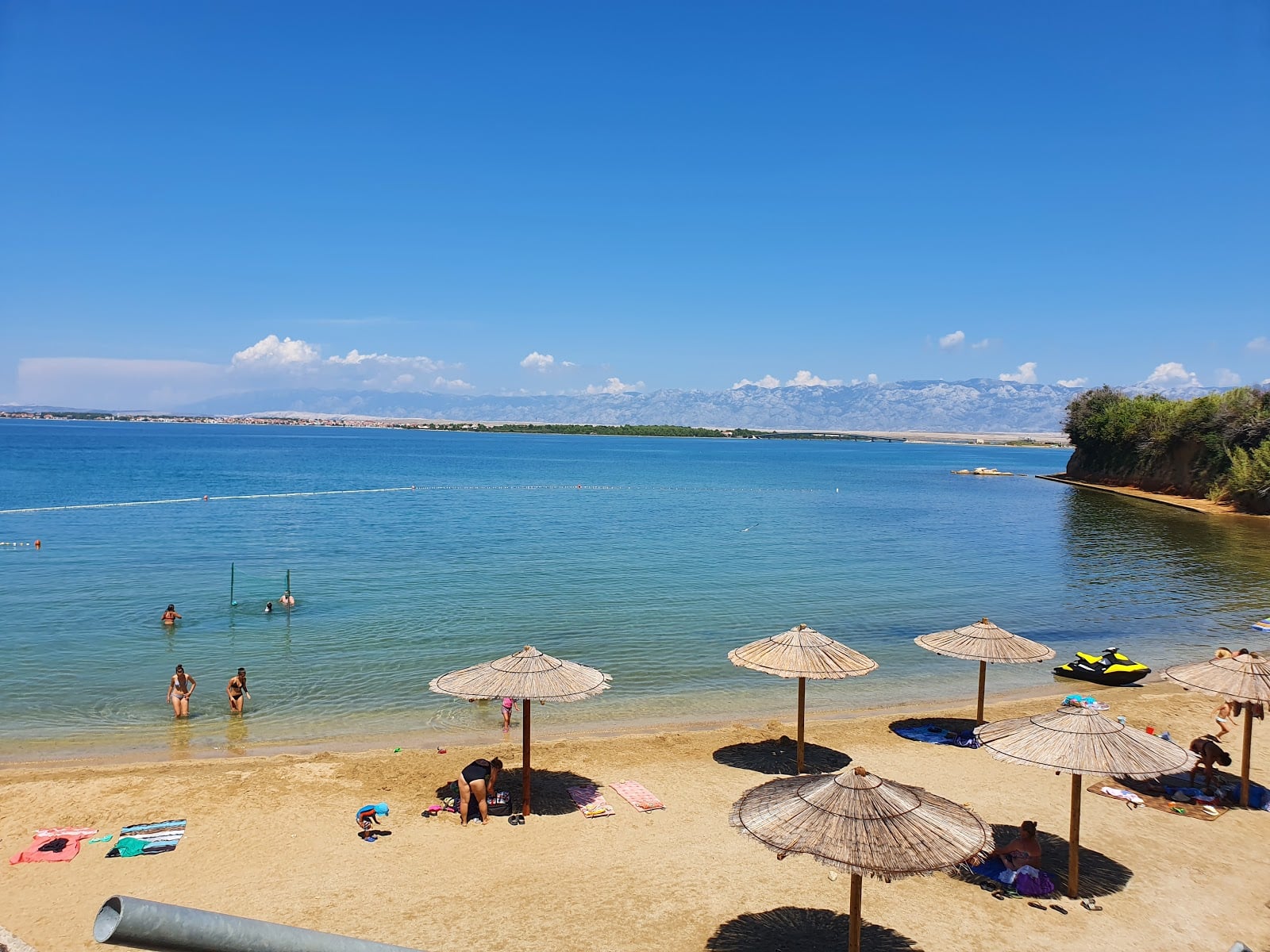 Seaward facing view of Privlaka Beach with sunbathers relaxing under wooden parasols