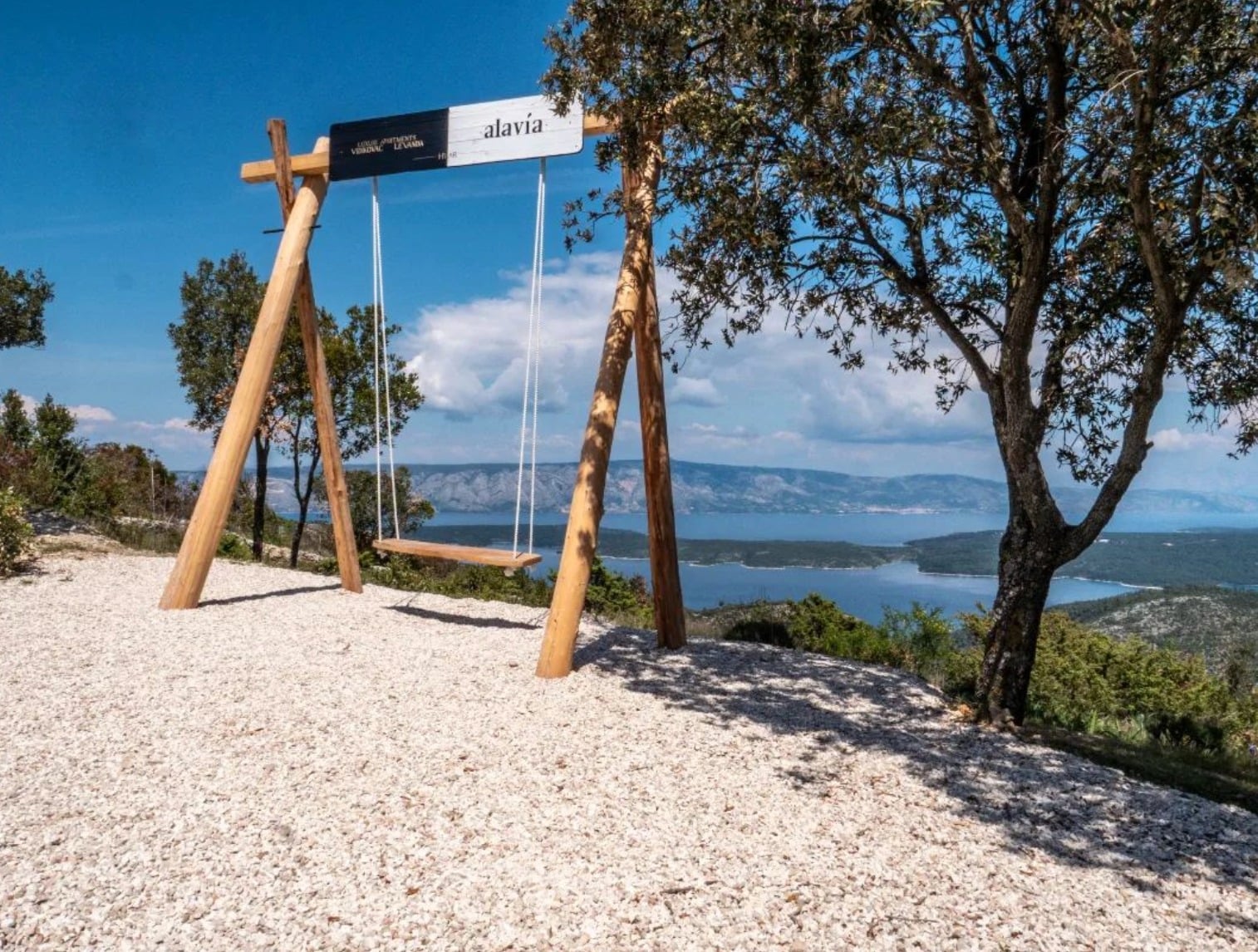 A wooden swing sits atop a hill above a panoramic view of the Stari Grad bay beneath